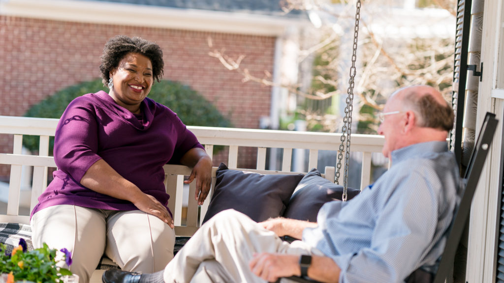 Photo of Stacey Abrams talking with a supporter on a front porch.