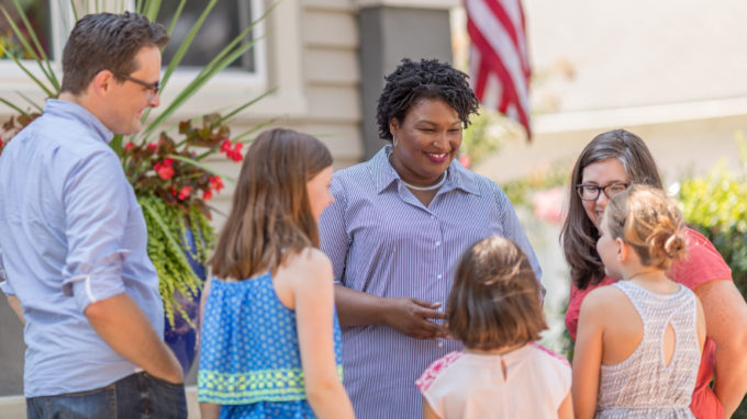 Stacey Abrams standing outside a house with a group of supporters.